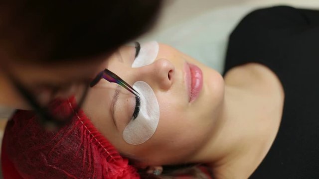 Close-up of professional stylist lengthening lashes for female client in a beauty salon.