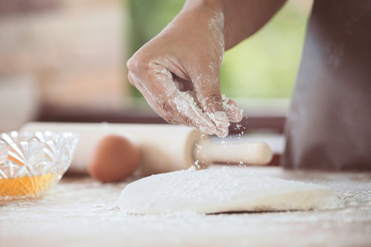 Woman hand preparing bread dough sprinkling white flour on dough for baking cookies in the kitchen in vintage color tone