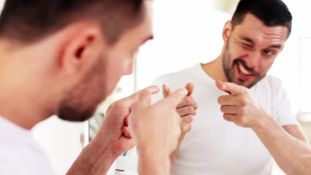 happy young man looking to mirror at home bathroom