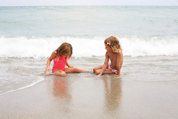 Two little girl sitting on the beach.