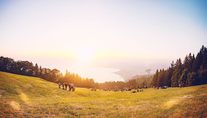 Menschengruppe auf einer Wiese mit Blick auf den Bodensee mit Sonnenuntergang