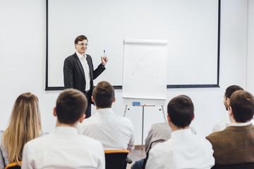 Business meeting at office. Handsome man presenting charts on whiteboard to team. Multi ethnic group of people