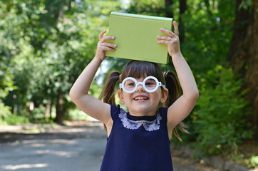 Fototapeta na wymiar Adorable little girl with two tails and white glasses is going to school. Happy girl with book