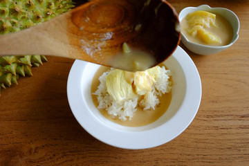 Pouring coconut milk on the sticky rice toping with durian on the wooden table