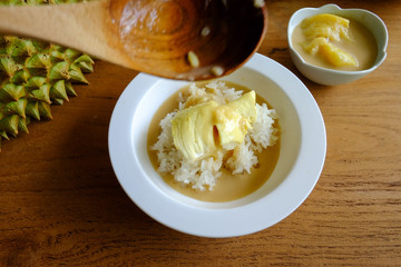Pouring coconut milk on the sticky rice toping with durian on the wooden table