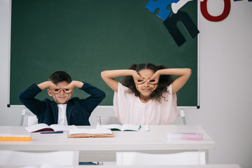 Cute multiethnic pupils having fun while sitting together at desk in class