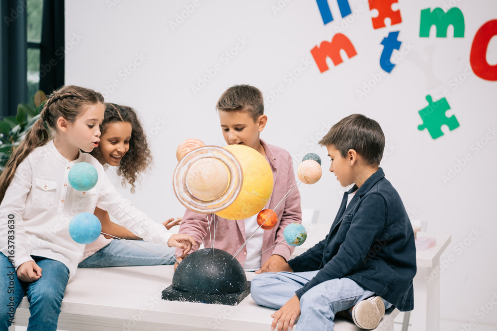 Wall mural multiethnic group of schoolchildren working with solar system model in classroom