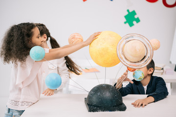 Multiethnic group of schoolchildren working with solar system model in classroom