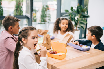 Multiethnic group of schoolkids eating lunch while sitting together at table