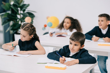 Cute little schoolchildren sitting at desks and writing in exercise books