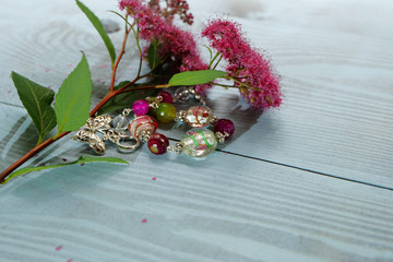 A glass bracelet and a branch of crimson flowers on a wooden blue background.