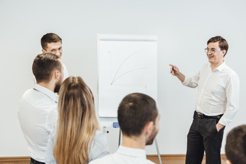 Business meeting at office. Handsome man presenting charts on whiteboard to team. Multi ethnic group of people