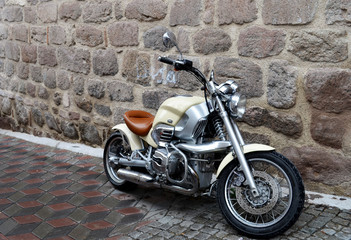 Beige motorbike in front of the stone wall. Rainy day.
