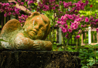 A cherub ornament rests peacefully among garden flowers