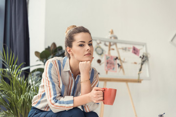 beautiful thoughtful businesswoman with coffee cup sitting in modern office