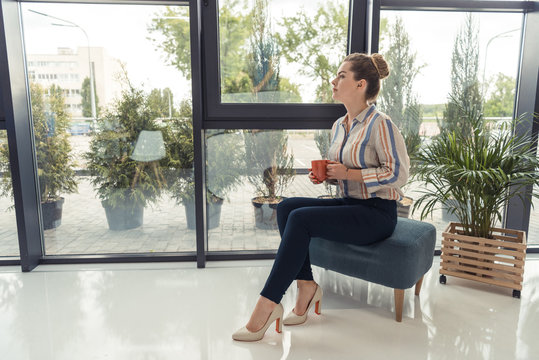 attractive thoughtful businesswoman on coffee break siiting at window in modern office