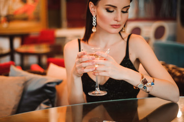 A beautiful girl drinks martini in the hotel lobby and is waiting for her young boyfriend