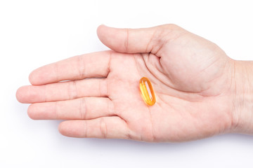 Close up yellow soft gel capsule in male hand with white background, concept of essential oil supplement intake.