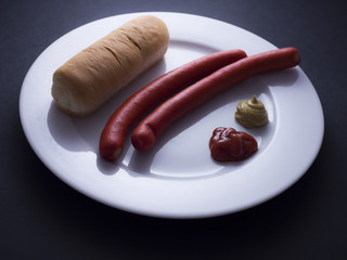Two red sausages from Denmark made from pork meat served on white plate with bread, ketchup and mustard sauce. Isolated on black background 