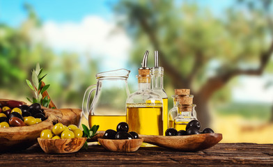 Freshly harvested olives berries in wood bowls and pressed oil in glass bottles