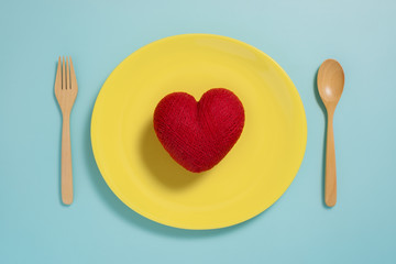 Flat lay of red heart on yellow plate with fork on pastel blue color background