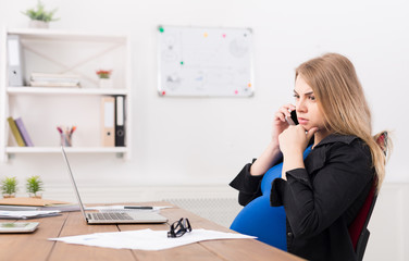Obraz premium Pregnant business lady at work talking on phone