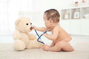 Cute little baby with stethoscope and toy bear playing at home