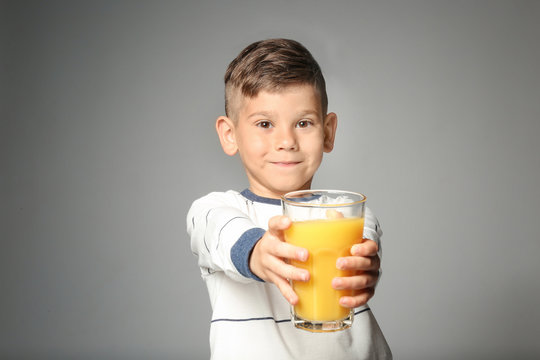 Cute little boy with glass of juice on grey background