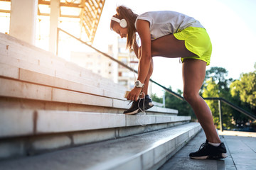 Young woman jogging with earphones tying shoelaces