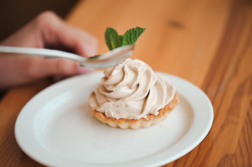 Woman eating a cake of cottage cheese in a ceramic plate with a spoon on a wooden table