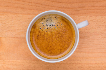 Hot black coffee with foam bubbles in white cup with wooden board in background, morning coffee concept.