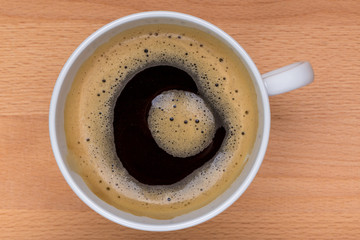 Detail of hot black coffee with some foaming on top in the white cup and wooden board in background, morning coffee concept.