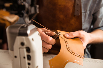 Man artisan sewing leather shoes indoors
