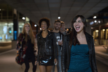 Group of cool friends going out at night walking in city street happy
