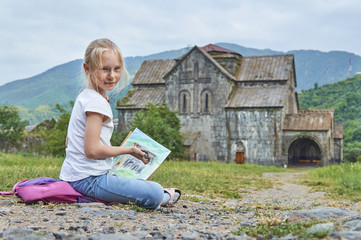 Blonde schoolgirl draws by chalk on the open air sitting on the ground in an ancient armenian...