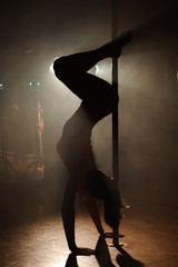 Naklejka na ściany i meble Young sexy woman exercise pole dance on a dark background