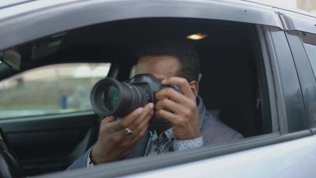 Private detective man sitting inside car and photographing with dslr camera