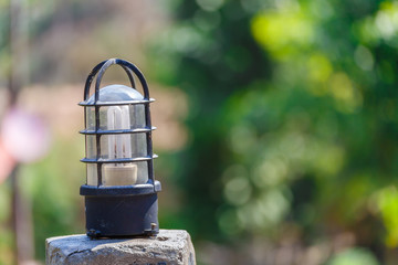 Light bulb on concrete pole with green bokeh background.