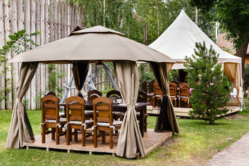 Two canvas tents with wooden tables and chairs. Vintage design of the restaurant in the forest.