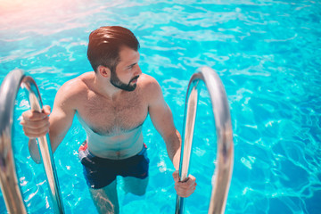 Summer photo of muscular smiling man in swimming pool. Happy male model in water on summer...
