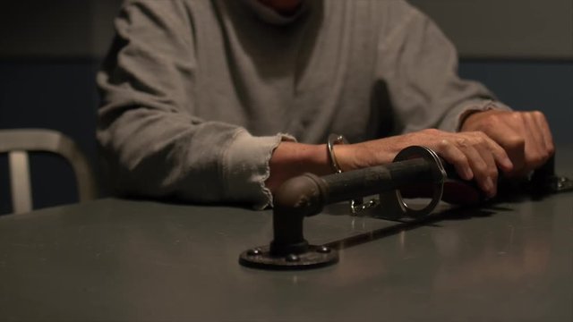 MAN FIDGETS WHILE HANDCUFFED TO TABLE, CLOSE UP