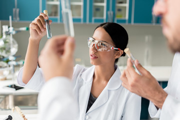 Young scientists in white coats examining test tubes with reagents in chemical lab