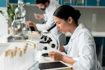 Concentrated young female scientist working with microscope in chemical lab