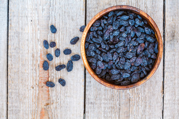 Fototapeta na wymiar Black raisins in a wooden bowl. Healthy light snack, dried fruit, top view.
