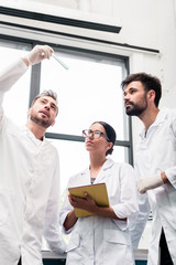 Obraz premium Professional young scientists in white coats examining test tube and using digital tablet