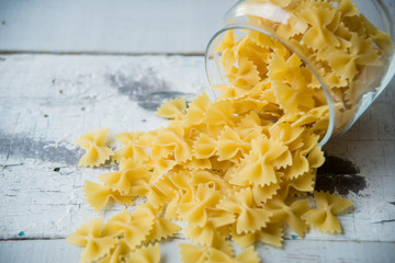 Pasta in the form of bows scattered from glass jar. Italian handmade pasta on the old background.