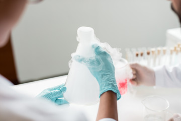 Fototapeta premium Close-up partial view of scientists making experiment with reagent and flasks