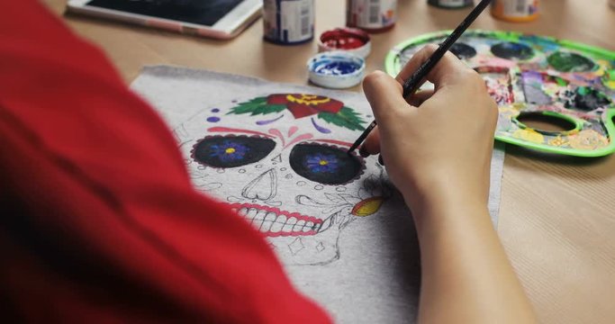 Close-up drawing on clothes. Girl draws on material mexican mask. White T-shirt with a pattern. mexican mask. colorful pattern in process. Creative time in the art studio
