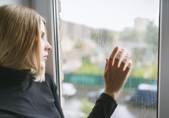 Sad woman looking through the glass window with a rain drops.