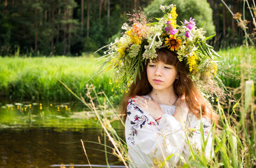 Beautiful young girl in a wreath from wild flowers near the river.